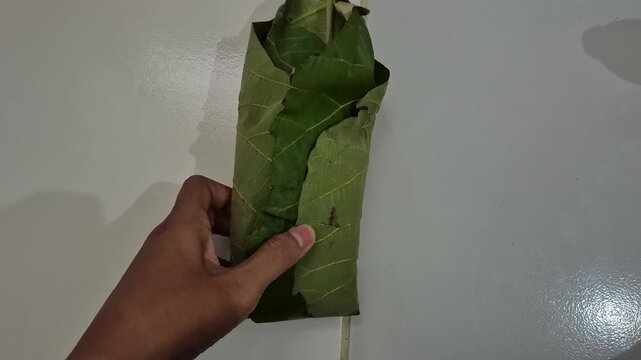 Traditional Indonesian Nasi Berkat wrapped in Teak Leaf and Banana Leaf on white floor