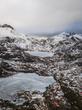 Aerial view of icy waters nestled amongst snow-dusted rocks beneath a moody sky, Tind, Nordland, Norway.