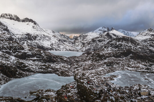 Aerial view of snow-dusted peaks and frozen lakes under a dramatic sky create a serene yet rugged landscape, Tind, Nordland, Norway.