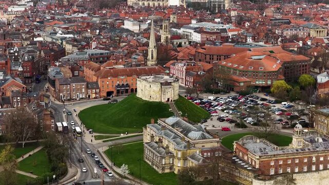 Aerial drone footage of Clifford Tower in the city of York in Yorkshire UK showing circular structure grass mound surrounding roads and car park captured directly from above in the spring time