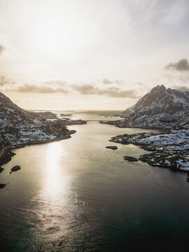 Aerial view of the bridge connecting snowy isles, with dark waters reflecting the sky, a scene of stark beauty and serene contrast, Kakernbrua, Nordland, Norway.