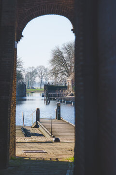Quiet waters reflect bare trees through an ancient archway.
