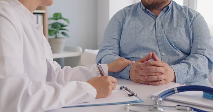Compassionate doctor and fat overweight patient meet in medical clinic to discuss healthcare goals and checkup plans. Physician consoles man during consultation. Obesity counseling