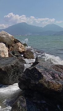 Crystal-clear sea waves gently washing over coastal rocks with a scenic mountain horizon in the distance. Serene seaside atmosphere with natural textures and refreshing summer vibes. 