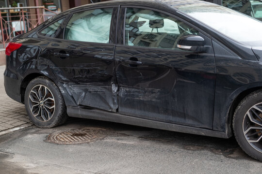 Black sedan with severe side collision damage, dented doors and deployed curtain airbags after a traffic accident.