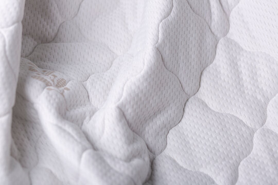 Close-up of quilted mattress fabric in soft beige. Highlights texture, stitching, and delicate material suitable for mattresses and bedding.