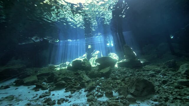 Sunlight beams penetrate clear water illuminating snorkeler above rocky cave floor in Cenote Dos Ojos, Quintana Roo, Mexico