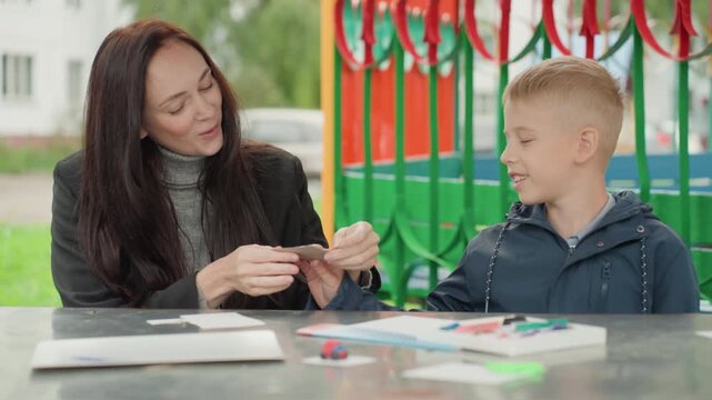 Youngsters and instructor crafting personalized artistic cards in sunshine. Teenagers and their coach designing custom handmade cards amid vibrant art supplies outdoors in bright sunshine