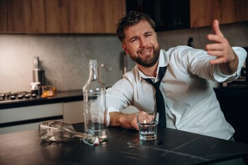 Obraz premium Smiling man in a white shirt and black tie gestures while sitting at a kitchen table with an empty bottle and glass, conveying a relaxed atmosphere and social interaction