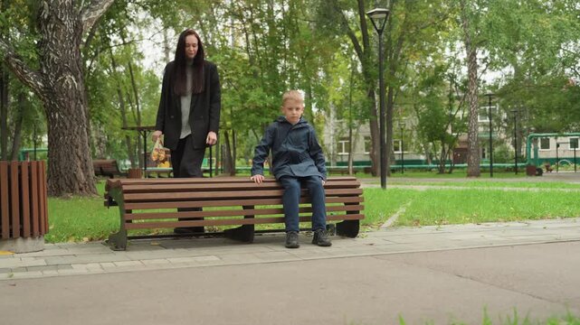 White guardian sits with boy on park bench preparing for back to school, sharing snack and warm drink from thermos, quiet morning conversation, leafy trees and gentle reassurance, comforting routine