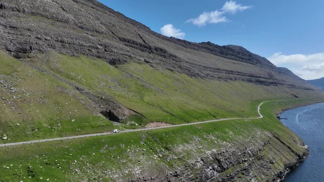 Drone shot of vehicle driving on narrow road on the Faroe Islands