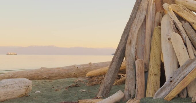 Driftwood teepee fort on a sandy beach at sunset with ocean view