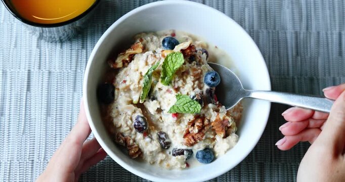 Hand stirring overnight oatmeal with fruits and nuts in white bowl. Healthy breakfast preparation concept. Wholesome, natural food, slow motion.