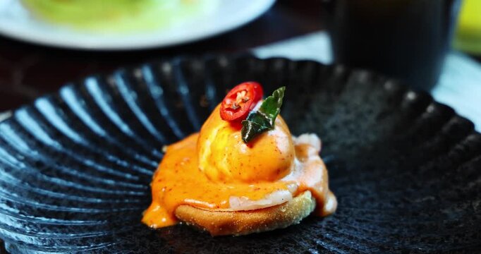 Gourmet benedict egg with spicy hollandaise sauce served on a dark textured plate. Fusion cuisine concept. Elegant, delicious, and appetizing food presentation.