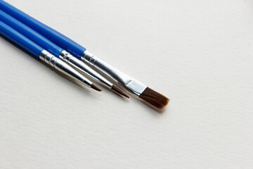 Fototapeta premium Three paintbrushes with blue handles arranged on a blank canvas