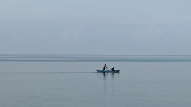 Two people are rowing a small boat across a calm body of water on a cloudy day.
