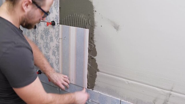 Worker Laying Ceramic Tiles on the Wall. Repairman Placing White Gray Square Tiles, Applying Adhesive. Builder Installing Tile Using Leveler, Tile Leveling Clips. Tiling. Finishing Repair Work. 4K