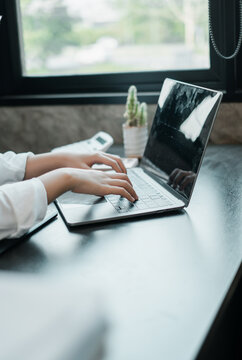 Close-up of hands typing on a laptop in a bright, modern office setting with minimalist decor and natural light.