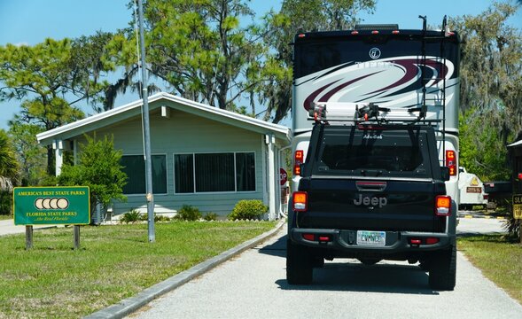 Bradenton, Florida, U.S.A - March 27, 2026 - The rear view of a large Tiffin Allegro motorhome towing a dark Jeep Wrangler into the entrance of the Lake Manatee State Park