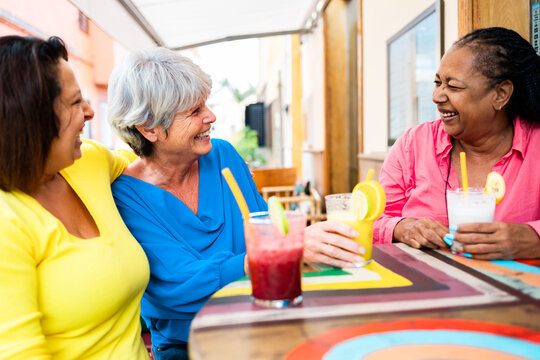 Multiracial senior friends having fun outside bar restaurant while drinking healthy smoothies - ugc content
