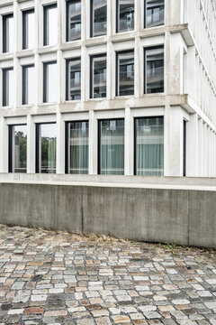 Empty pavement under a modern urban facade with windows and wall creating ordered architecture patterns and subtle wayfinding guidance in city streets