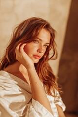 Naklejka premium Vintage style portrait of a woman with long brown hair, wearing a white blouse, softly illuminated by warm light against a textured background