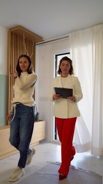 Young female client entering new property for sale with realtor. Professional real estate agent presenting contemporary apartment with wooden interior to prospective homeowner