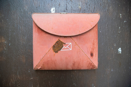 Old red metal mailbox shaped like an envelope mounted on a dark wall.