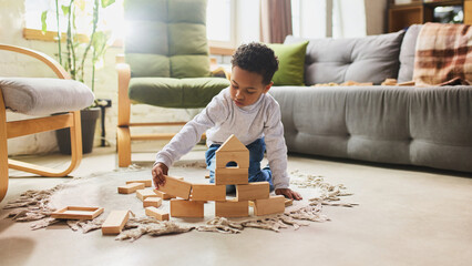 Child building wooden block house on floor in cozy living room environment. Concept of creativity, imagination and construction play supporting early development. © master1305