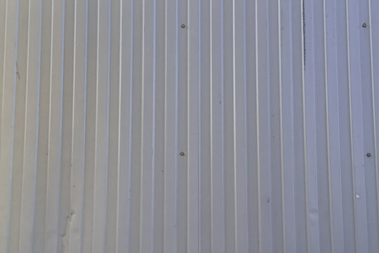Minimalist texture of a grey corrugated metal wall panel with vertical lines and rivets, industrial steel siding background in soft daylight