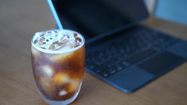 Close-up of refreshing iced Americano coffee with condensation on glass next to tablet and pink rose for lifestyle and break time concept