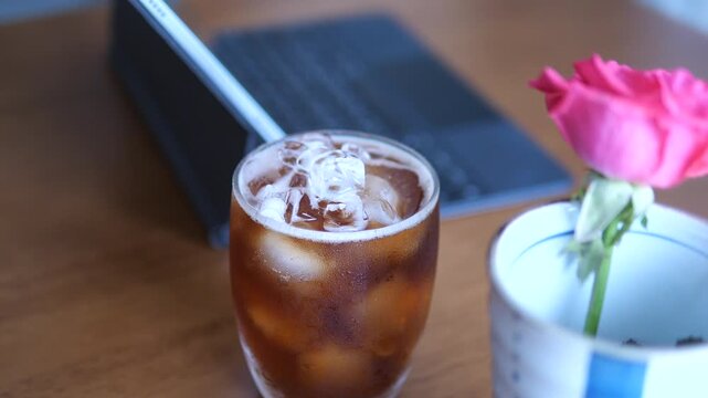 Close-up of refreshing iced Americano coffee with condensation on glass next to tablet and pink rose for lifestyle and break time concept