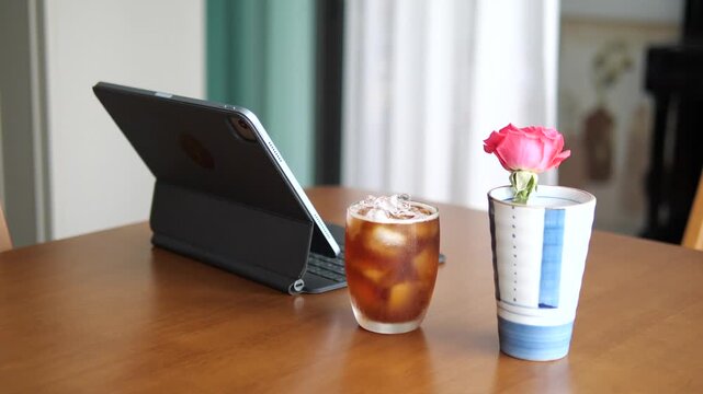 Close-up of refreshing iced Americano coffee with condensation on glass next to tablet and pink rose for lifestyle and break time concept