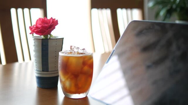 Close-up of refreshing iced Americano coffee with condensation on glass next to tablet and pink rose for lifestyle and break time concept