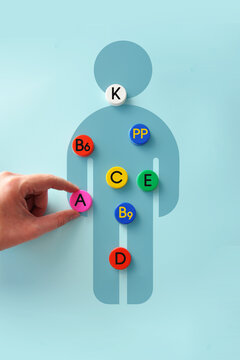 Human body silhouette with vitamin icons, hand placing vitamin A, health and nutrition concept