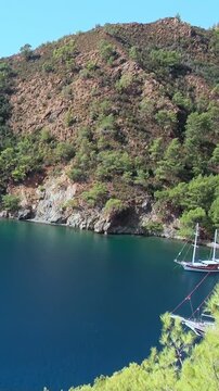 Lone sailboat graces deep blue Aegean Sea, cradled by majestic, pine-clad slopes of Babadag Mountain. This tranquil Fethiye bay, near Oludeniz, offers serene daytime escape under brilliant sky.