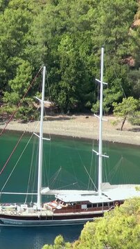 Sunlight illuminates a grand gulet gently anchored in the stunning Oludeniz bay, Fethiye, Turkey. Emerald Aegean waters softly lap at the pristine, forested coast beneath the watchful Babadag Mountain