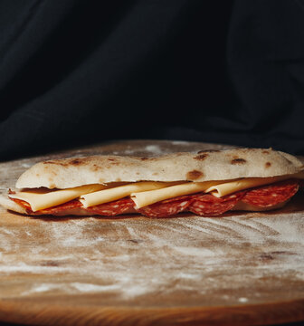 Artisanal pepperoni and cheese sandwich made with Italian saltimbocca bread served on a rustic floured wooden board.