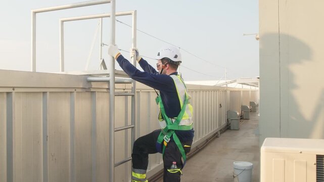 Two industrial engineers in safety helmets and harnesses standing on a rooftop mechanical platform at a large industrial facility with solar panels.