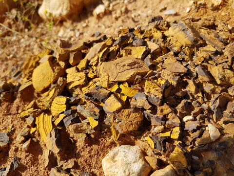 Broken limonite ore pieces, showing vibrant yellow and brown textures, lay scattered on the earthy quarry ground, revealing raw mineral beauty