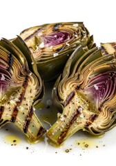 Obraz premium Grilled artichoke halves are seasoned with sea salt and drizzled with olive oil against a white background.