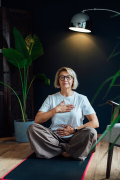 Middle aged woman practicing mindfulness and Pranayama breathing exercises in cozy space. She appears centered and serene. Meditating, relaxed, eyes closed. Mental health and well being concept