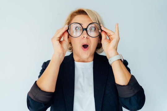 Middle aged surprised shocked fun 50's business woman touch specs, looking through big round glasses with open mouth isolated on white background. Wow expression. Human emotions, facial expression.