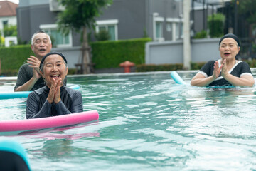 Fototapeta premium Smiling young woman in swimsuit using foam noodle for fitness training. Joyful intergenerational group exercising together outdoors to maintain good health and wellbeing.