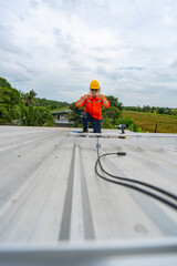 Obraz premium Technician in safety uniform and helmet kneeling on a rooftop, using a drill for precise installation work. A scene highlighting safety, professionalism, and technical expertise in construction.