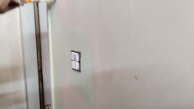 Worker painting wall edge near door frame and switch panel with brush and roller