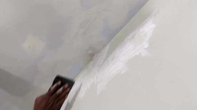 Worker sanding ceiling after putty application to prepare smooth surface before paint