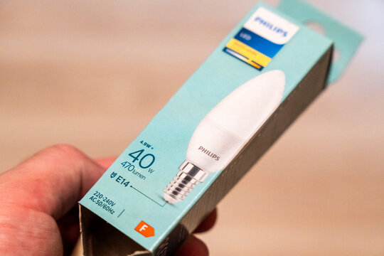 Warsaw, Poland - April 9, 2026: A hand holds a Philips LED light bulb packaging, showcasing its wattage and energy efficiency, suitable for various home and office lighting solutions.