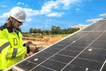 A solar technician in a high-visibility jacket and helmet stands next to a solar panel, with a serene landscape featuring a pond and distant greenery under a partly cloudy sky. © ultramansk