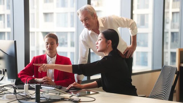 Three business professionals discussing project strategy around laptop in modern office meeting space with plants and collaborative atmosphere.